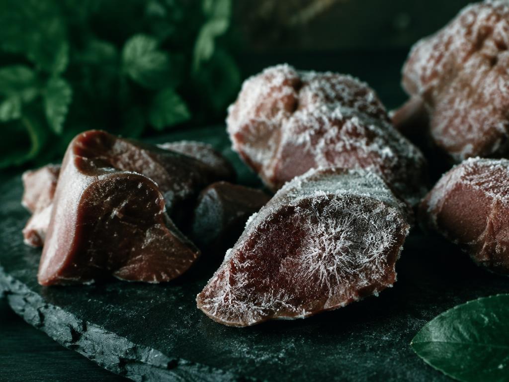 Freeze-dried organ meat pieces with frost crystals on dark slate